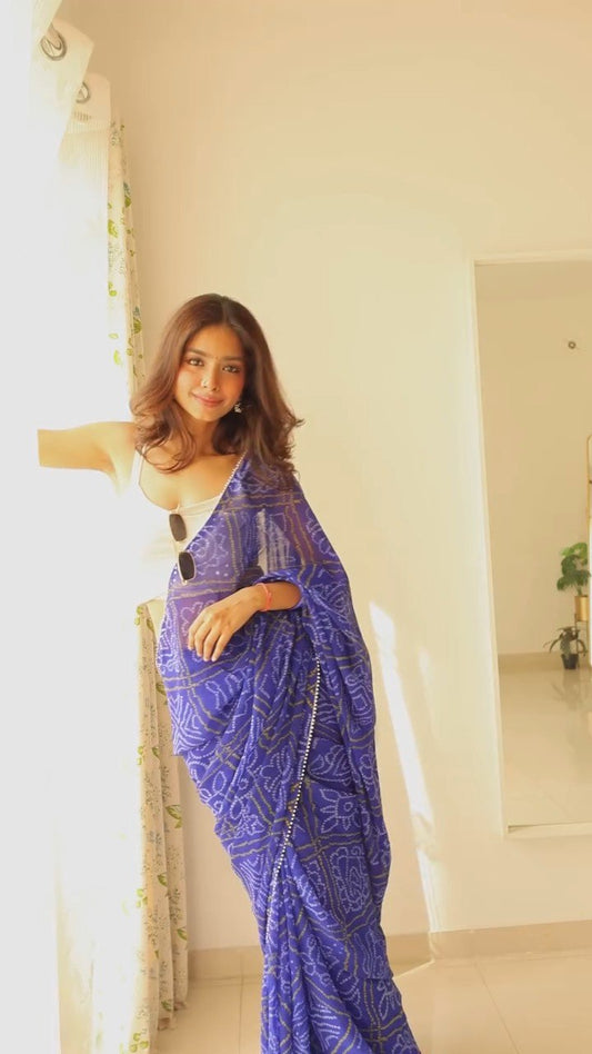 Woman leaning against window in stylish pre-stitched blue georgette saree.