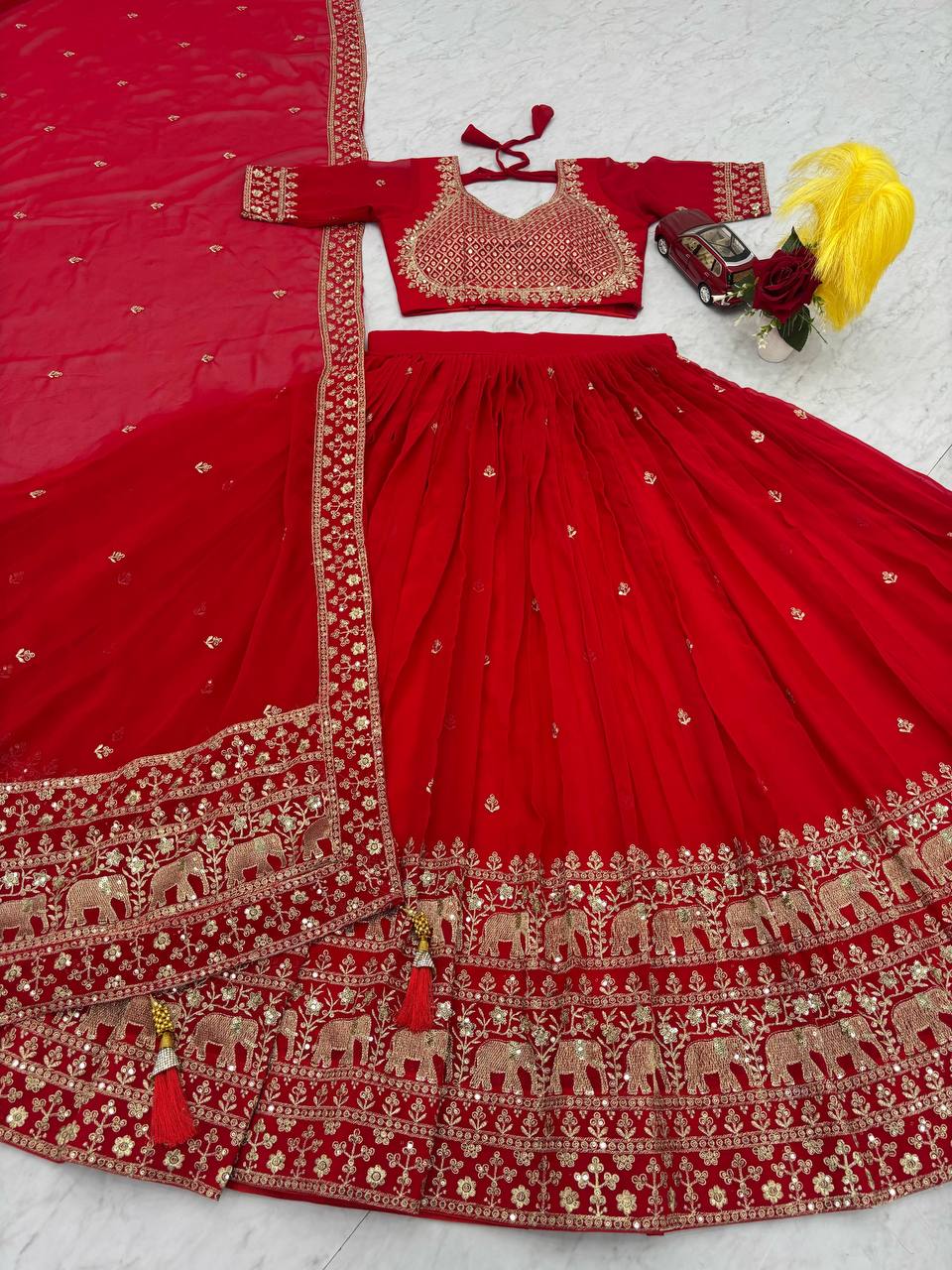 Red lehenga choli set with gold elephant embroidery and tassels.