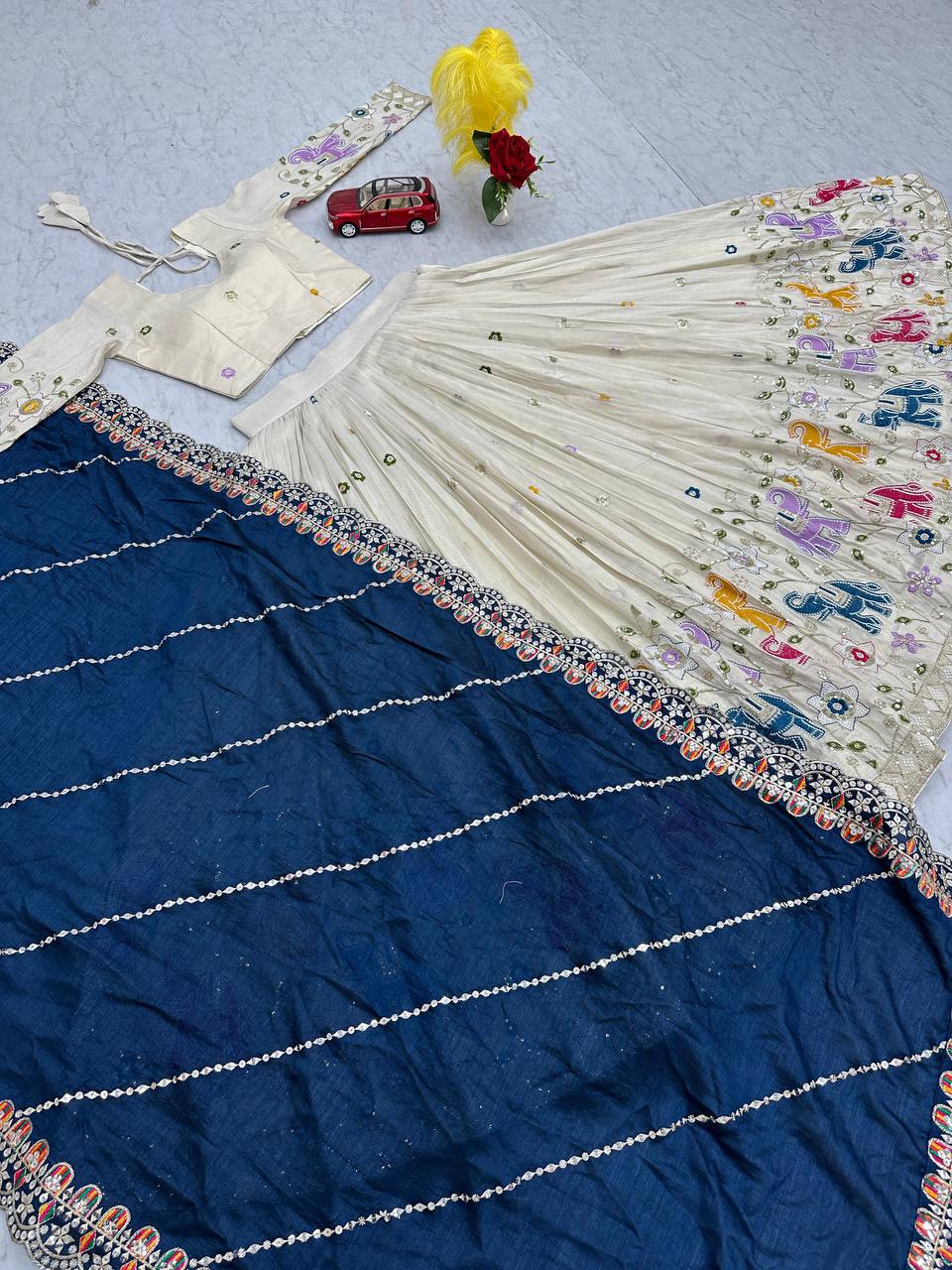 Overhead view of off-white lehenga choli with navy blue dupatta, showcasing embroidery.
