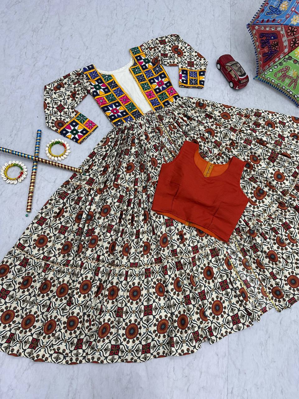 Flat lay of Kachchi Charm lehenga choli set with mirror work shrug, orange blouse, and flared skirt.