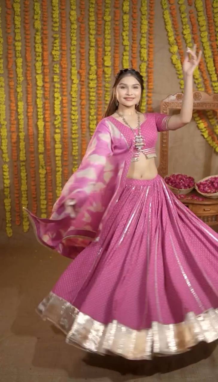 Woman twirling in a hot pink cotton lehenga choli set with gold border and printed dupatta, Navratri festive look.