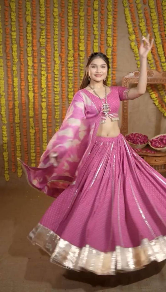 Woman twirling in a hot pink cotton lehenga choli set with gold border and printed dupatta, Navratri festive look.