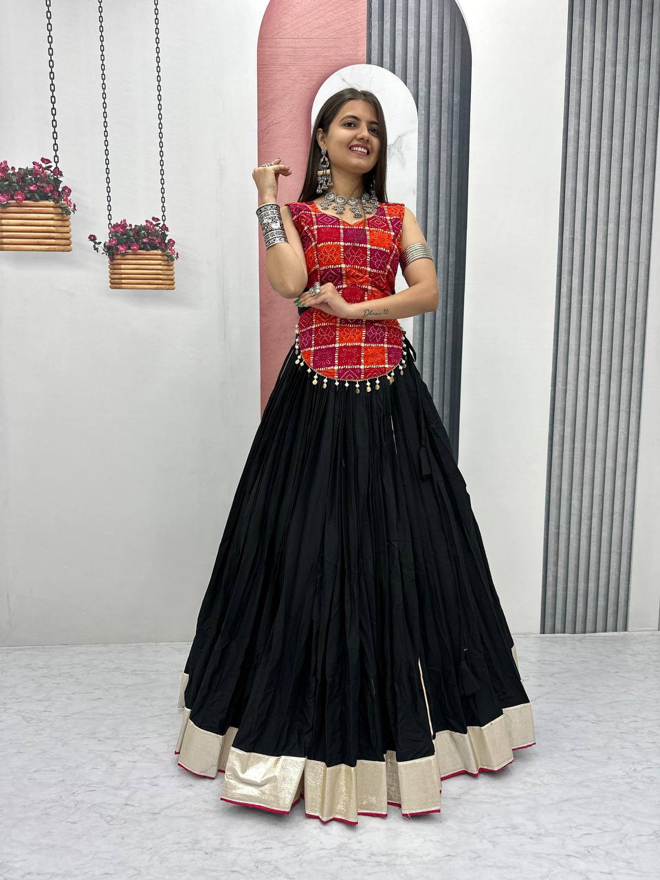 Smiling woman in black flared lehenga and red patterned choli with traditional jewelry, perfect for Garba.