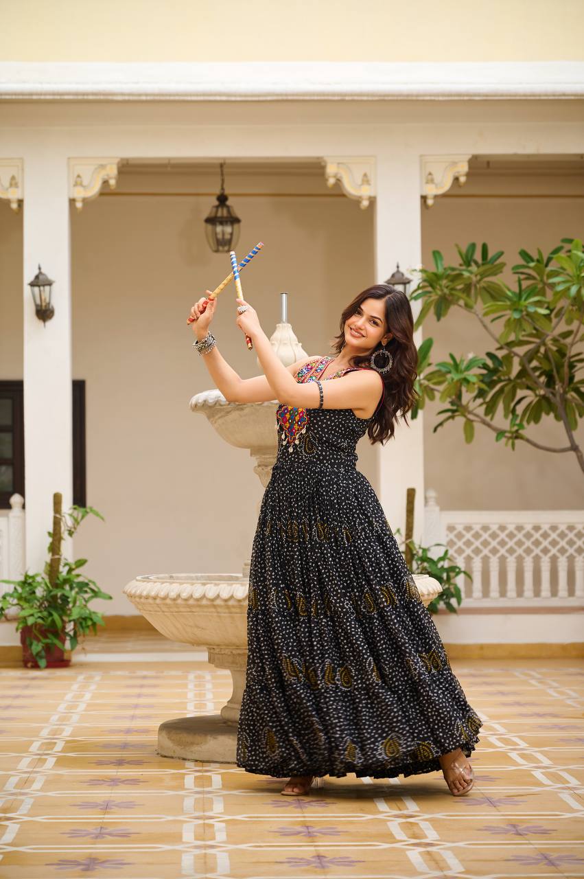 Woman in black Bandhani Gamathi gown dancing with dandiya sticks, festive setting.