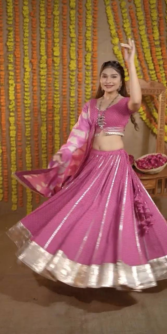 Front view of a woman spinning in a pink polka dot lehenga choli with metallic accents and matching dupatta.