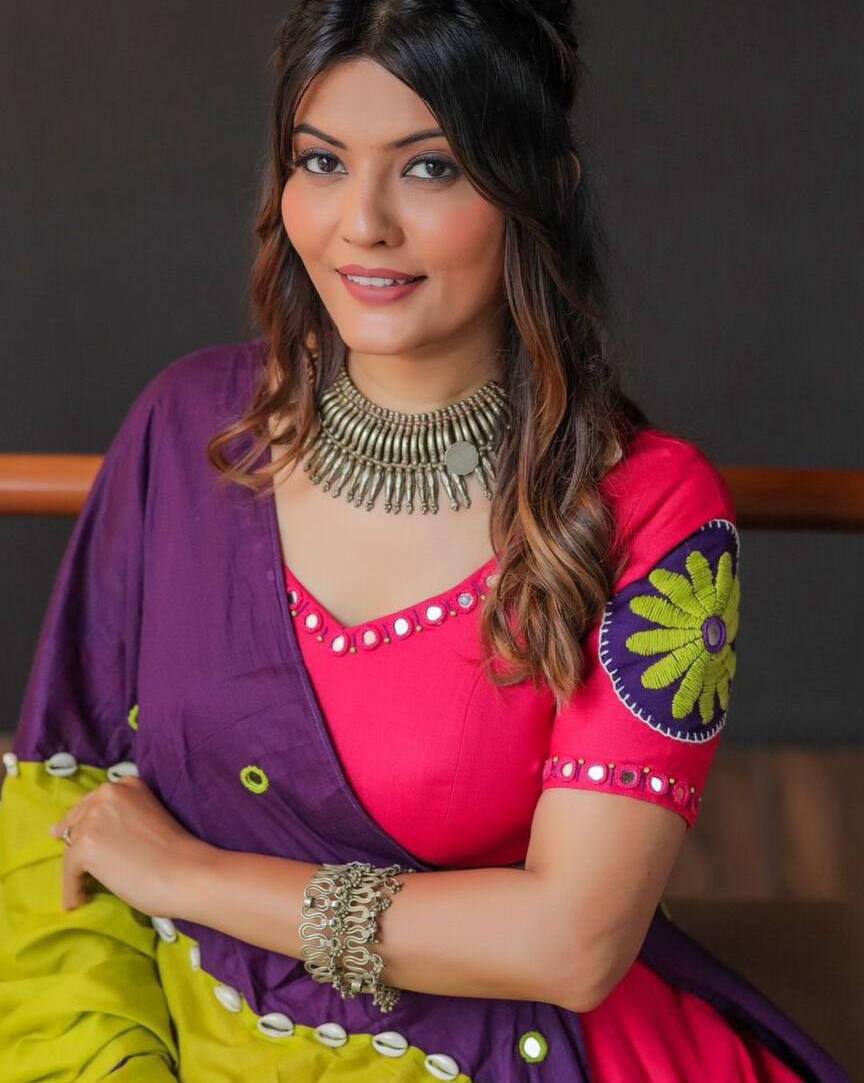 Close-up of embroidered lehenga choli in pink with mirror work and purple-yellow dupatta, styled with jewelry.