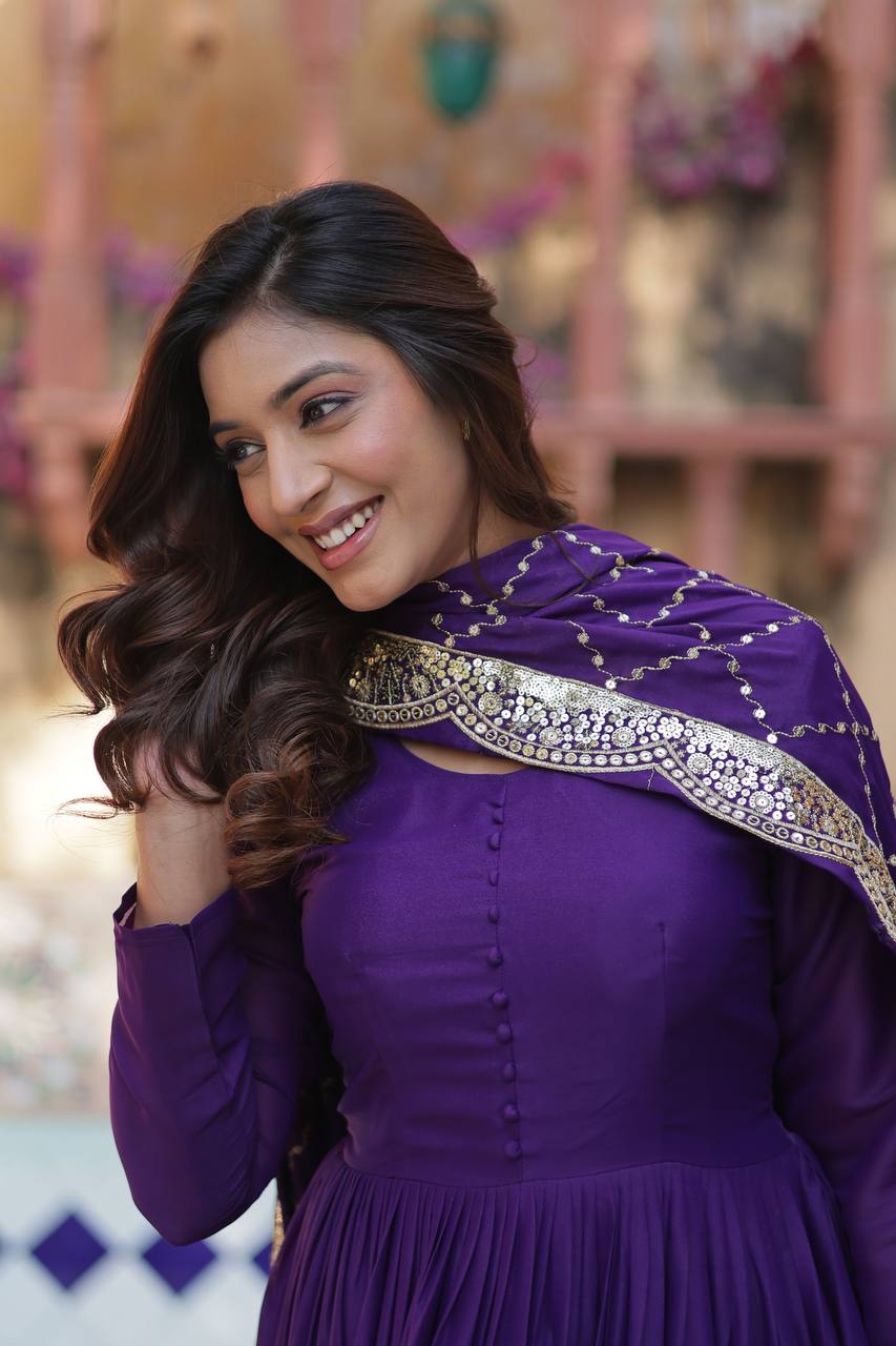 Close-up of a woman smiling, wearing a purple flared gown with embroidered dupatta.