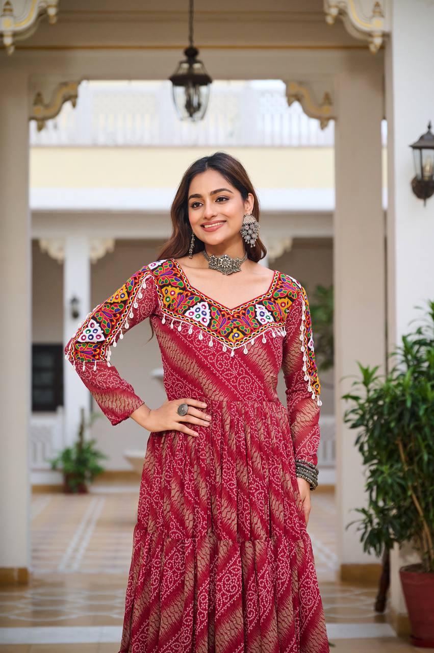 Model smiling in red Bandhni Gamathi work gown, showing mirror-embellished neckline and ethnic jewelry.