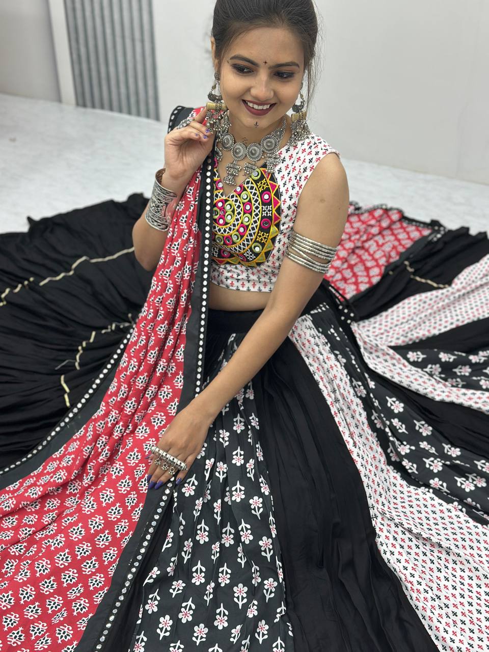 Woman smiling in cotton Navratri choli and twirl-ready lehenga, with red folk dupatta spread out.