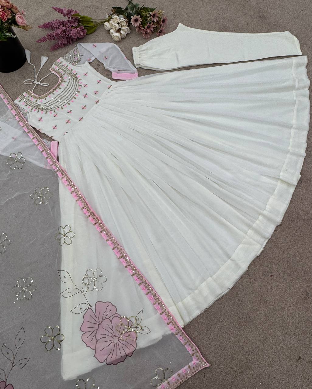 Embroidered glam gown set laid flat with off-white dress, churidar, and pink floral dupatta.