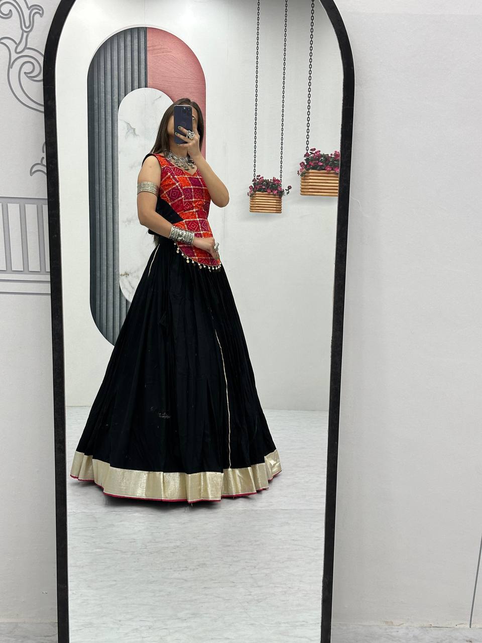 Side mirror shot of black lehenga and striking red choli with foil print, festive ethnic Garba outfit.