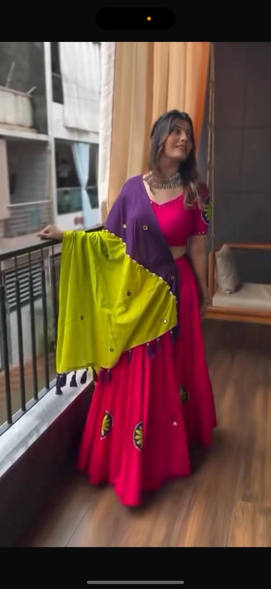 Woman on balcony wearing bright pink lehenga choli with purple and yellow embroidered dupatta, festive and elegant.