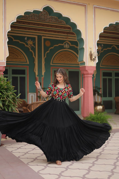 Maxi black Navratri gown with colorful embroidery, woman mid-twirl showing skirt's full volume.