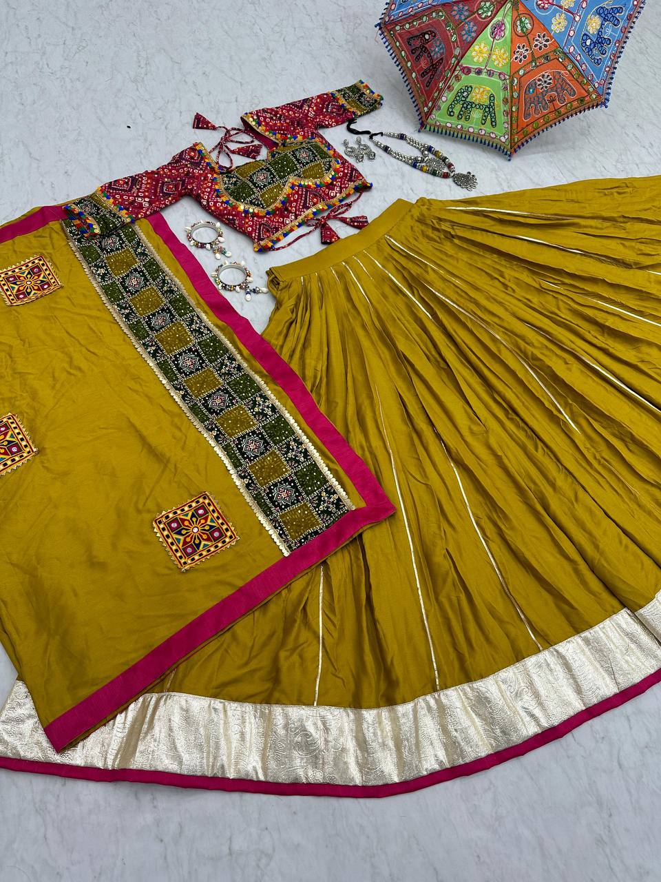Flat lay of golden lehenga choli, ornate dupatta, jewelry, and festive Navratri umbrella.