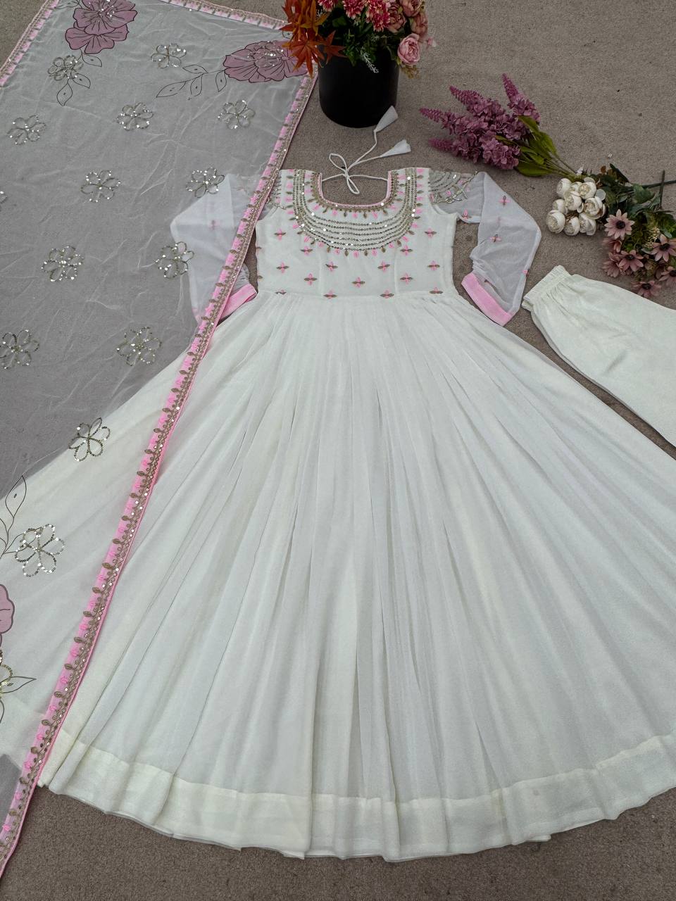 Full flatlay of off-white embroidered gown set with pastel pink floral dupatta and churidar.