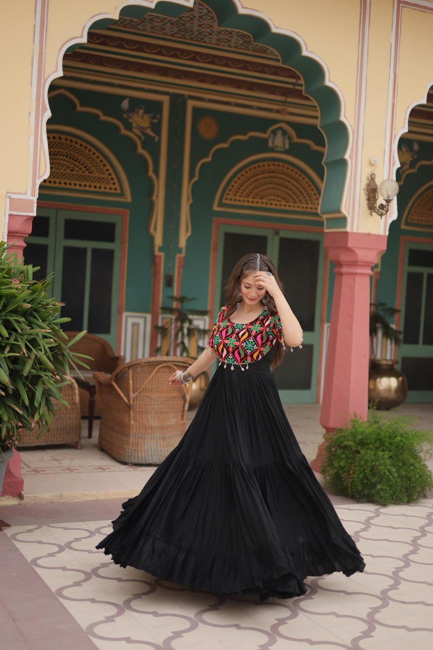 Dancing woman in maxi black Kutchi embroidered gown, flowing skirt and festival jewelry visible.