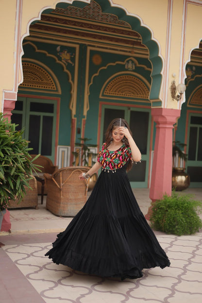 Dancing woman in maxi black Kutchi embroidered gown, flowing skirt and festival jewelry visible.