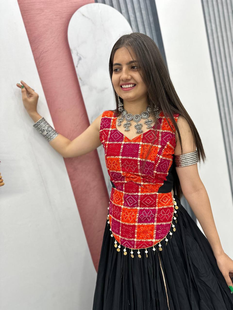 Happy woman modeling traditional vibrant choli and black lehenga, showcasing jewelry and festive look.