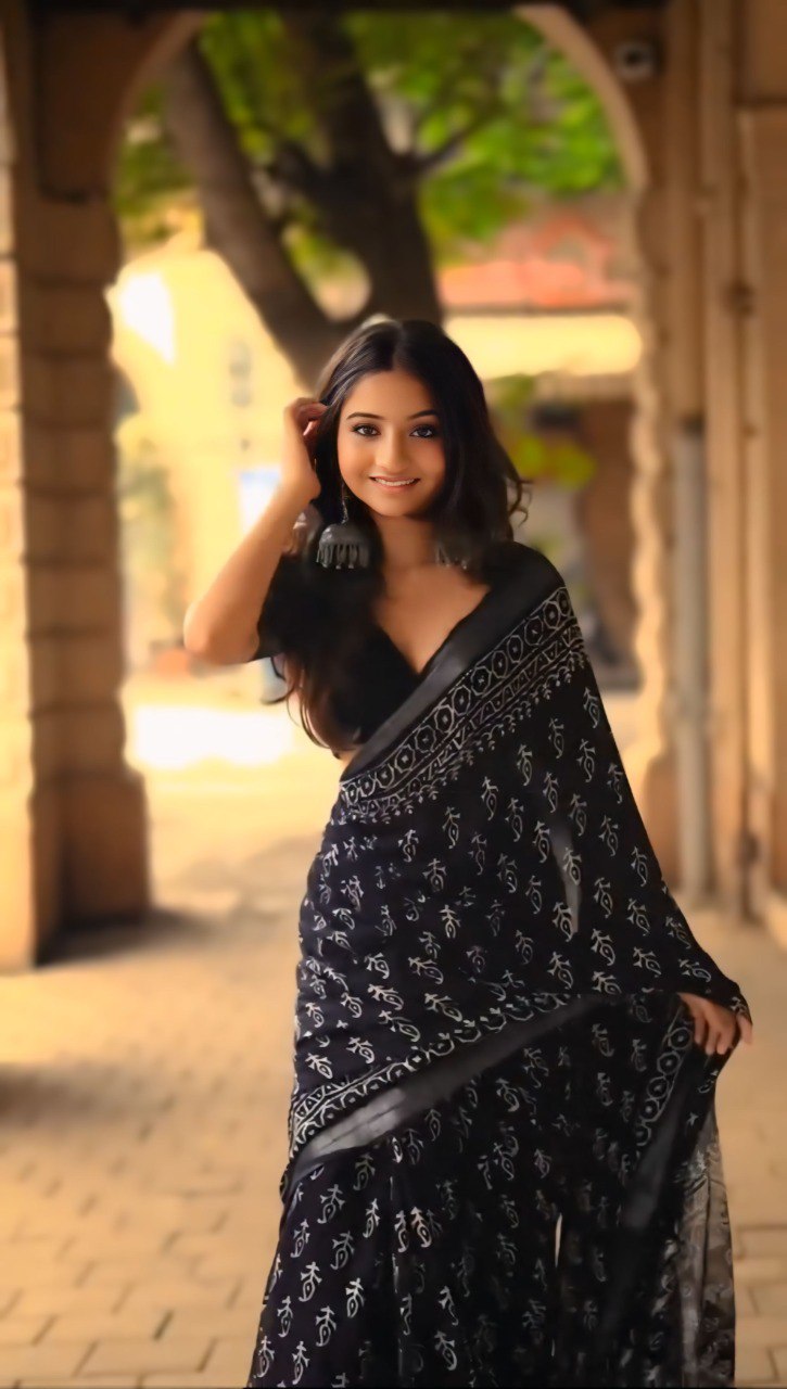 Smiling woman wearing a stylish black and white printed cotton saree outdoors.