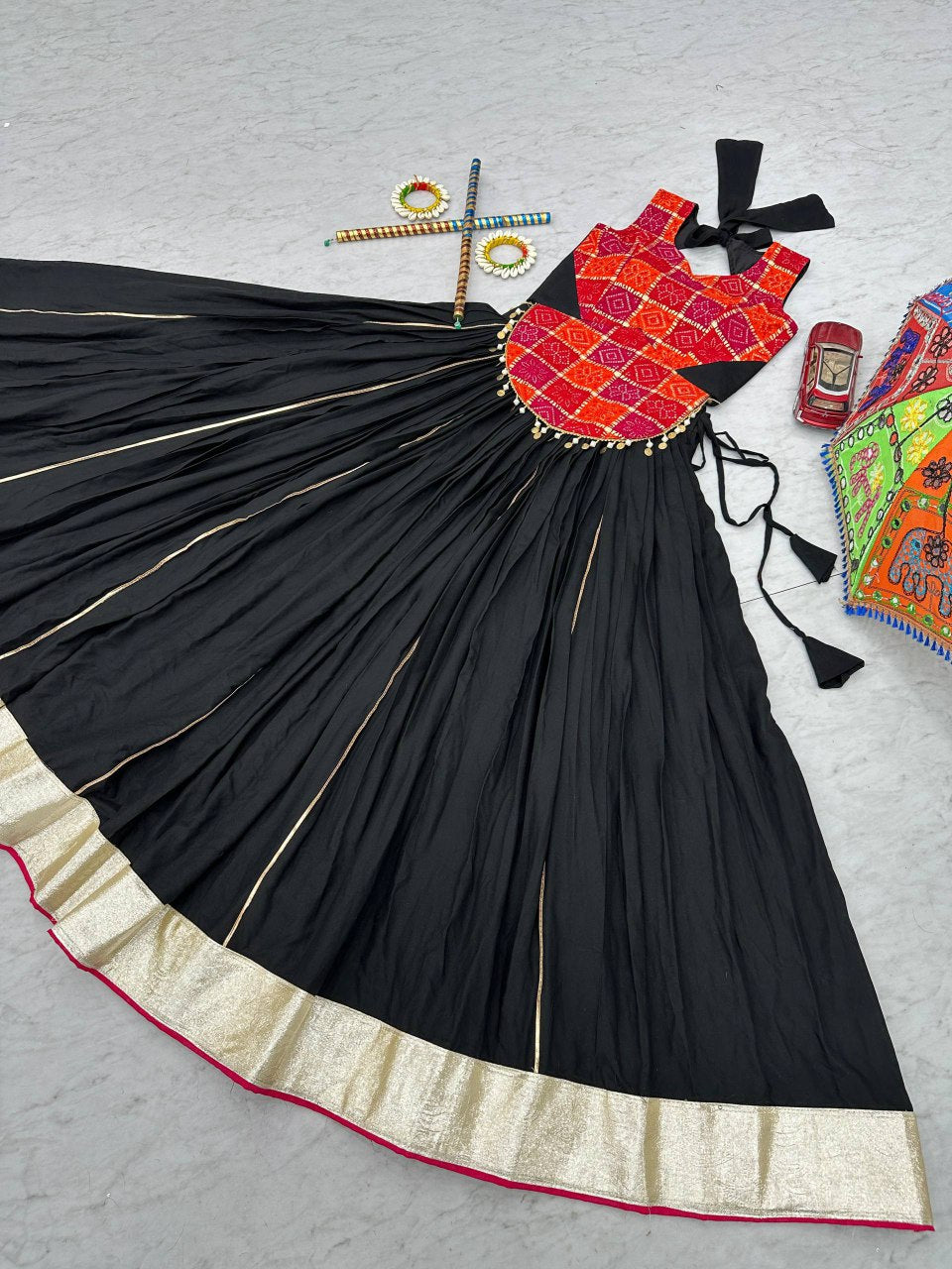 Navratri lehenga choli laid flat, black skirt with gold border, bright printed choli, dandiya and decor.