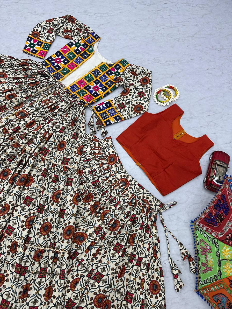 Flat lay of lehenga choli set, featuring mirror work shrug, orange blouse, and traditional festive skirt.