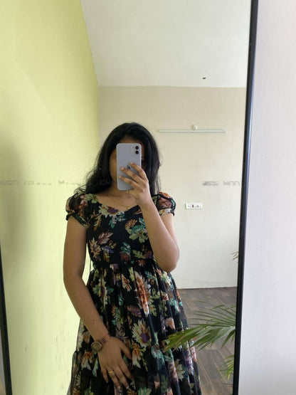 Close-up of the 'Floral Getaway' black dress with colorful floral print. Tiered design, short sleeves.