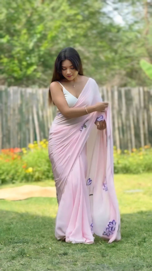 Woman in a draped pink georgette saree with delicate floral accents outdoors.