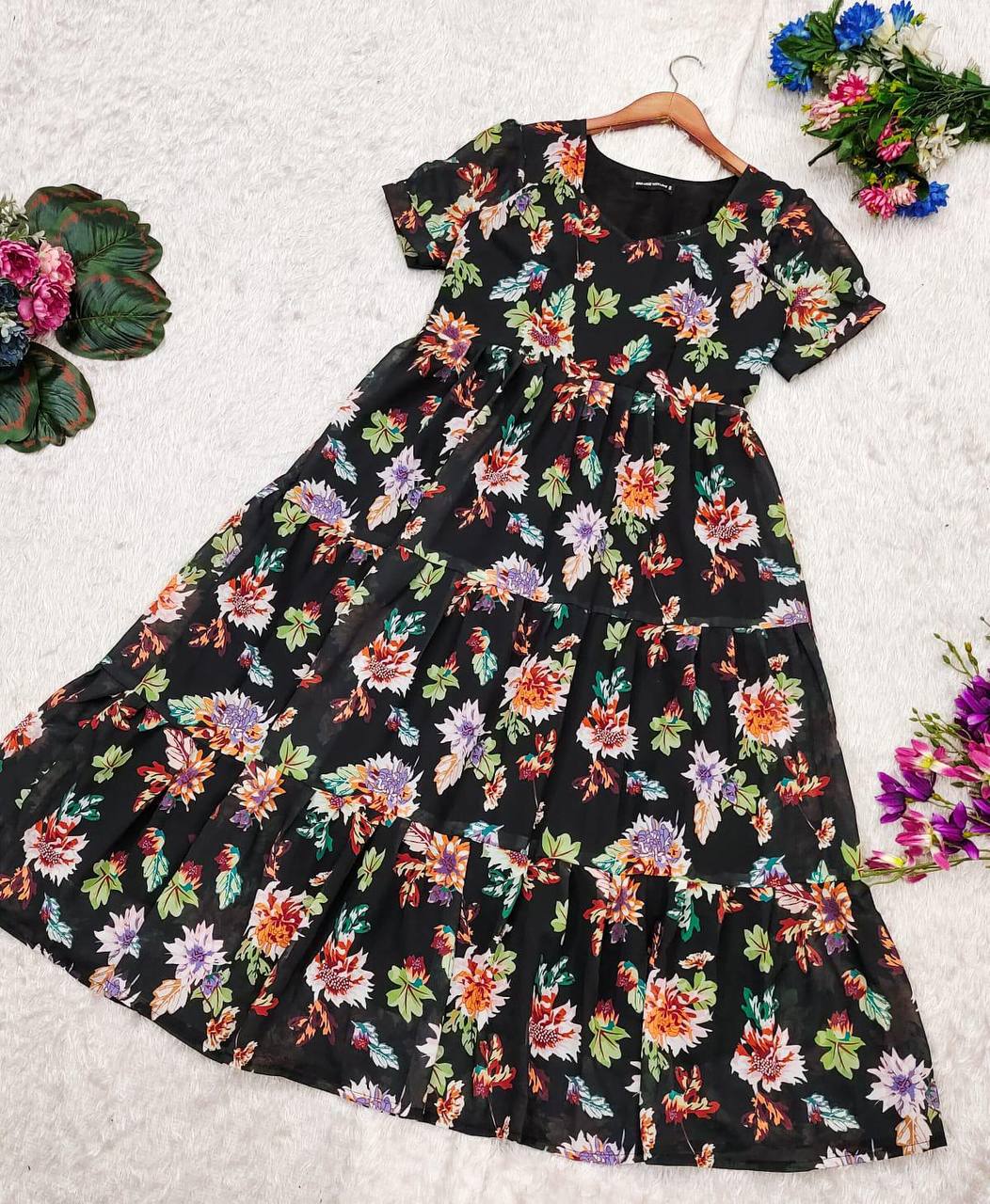 Flat lay of the 'Floral Getaway' dress, a black tiered dress with a bright floral print, on white.