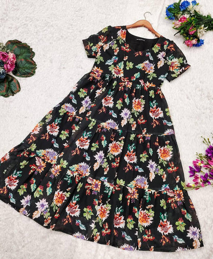 Flat lay of the 'Floral Getaway' dress, a black tiered dress with a bright floral print, on white.