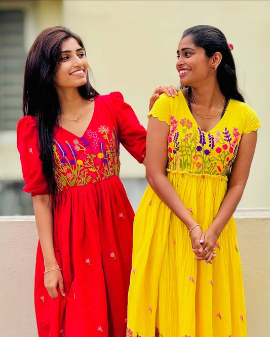 Two women smiling, wearing Rangbhoomi Floral Embrace dresses in red and yellow with chain stitch embroidery.